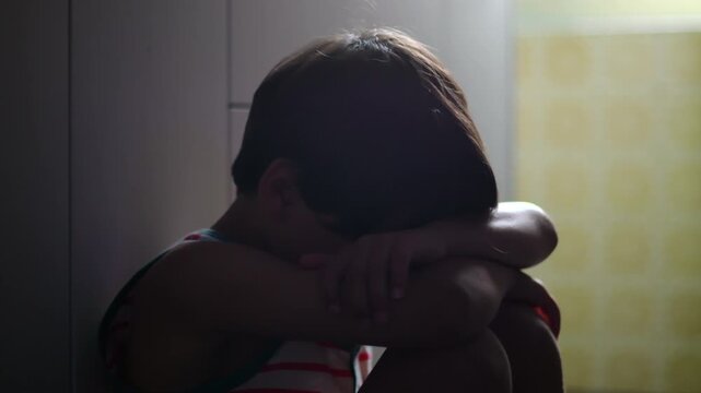 Child sitting curled in kitchen corner hiding face in arms expressing deep sorrow depression and emotional shutdown highlighting mental health struggle and isolation at home