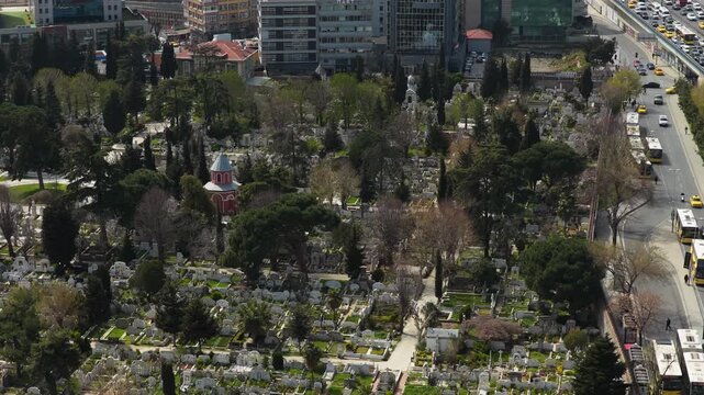 Aerial over Macka Cemetery in Istanbul showing tombs and grave sites next to busy road with traffic, surrounded by urban buildings city structures