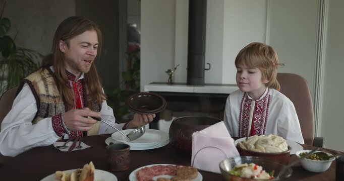 Man With Kid Boy Eat Food Lunch Dinner. Family in Ukrainian Traditional Attire Childhood. 4K 10-bit