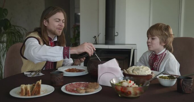 Man With Kid Boy Eat Food Lunch Dinner. Family in Ukrainian Traditional Attire Childhood. 4K 10-bit