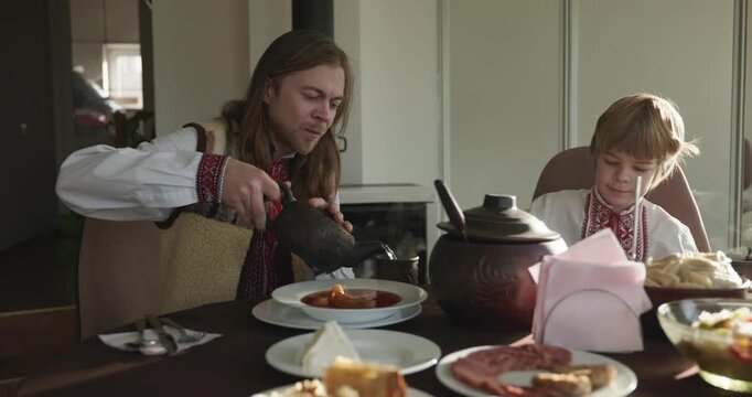 Man With Kid Boy Eat Food Lunch Dinner. Family in Ukrainian Traditional Attire Childhood. 4K 10-bit