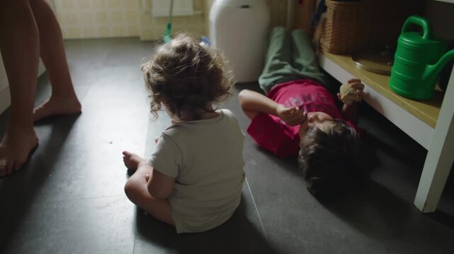 Mother preparing food at kitchen countertop then camera reveals children sitting on floor, everyday family life, multitasking parenting moment, domestic routine and natural home interaction
