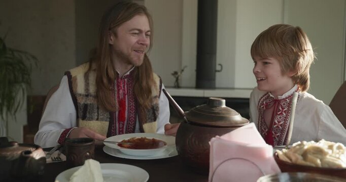 Man With Kid Boy Eat Food Lunch Dinner. Family in Ukrainian Traditional Attire Childhood. 4K 10-bit