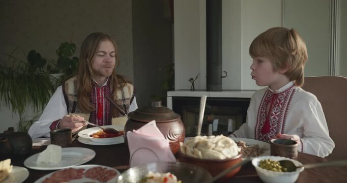 Man With Kid Boy Eat Food Lunch Dinner. Family in Ukrainian Traditional Attire Childhood. 4K 10-bit