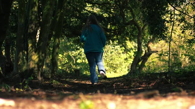 Woman running through woodland in dappled summer sunshine