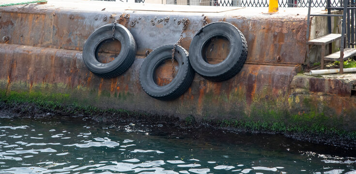 Tires hang on a rusty dock near dark green water at a port in the late afternoon