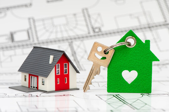 Ein Wohnungsschl&uuml;ssel mit Anh&auml;nger steht zusammen mit einem Modellhaus auf einem Bauplan,