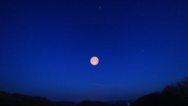 Full Moon, stars and planets above landscape silhouettes.