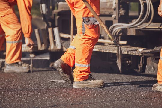 Construction workers working on a new asphalt layer on a public street.