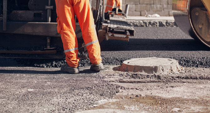 Construction workers working on a new asphalt layer on a public street.