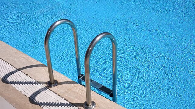 Top view of crystal clear blue water in swimming pool with stainless steel ladder. Professional maintenance, water treatment, luxury resort amenities, summer vacation and relaxation concepts