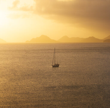 Aerial view of a lone sailboat on the calm ocean waters of Anse A La Mouche during a golden sunset with mountain silhouettes in the background Seychelles.
