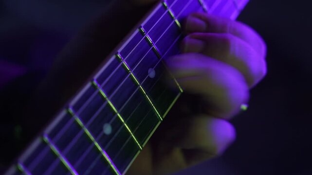 Close-up of a guitarist's hand playing chords on a fretboard during a concert with colored lights, fa01