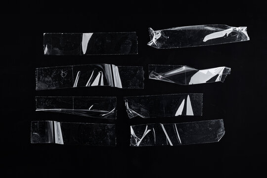 Collection of clear scotch tape pieces with wrinkled texture, air bubbles, and reflective glossy surface isolated on black.