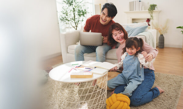 Asian father and Caucasian mother laughing and teasing little daughter while sitting on a sofa