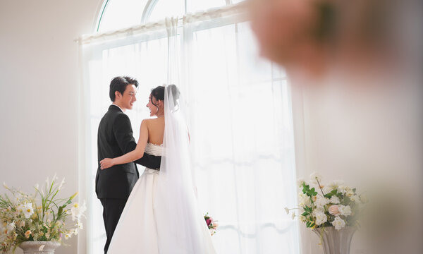 Asian wedding couple embracing and looking at each other by window