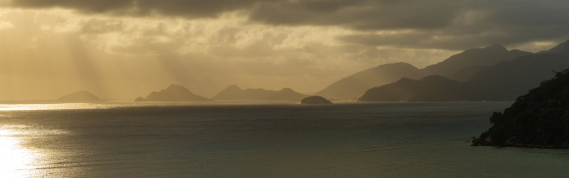 Aerial view of sunbeams breaking through dramatic clouds over the turquoise waters of Anse A La Mouche bay and silhouetted tropical islands Seychelles.