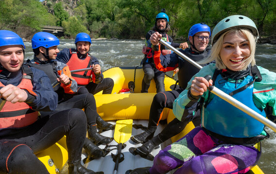 Rafting - six excited people with water gear in an inflating boat rowing down a river