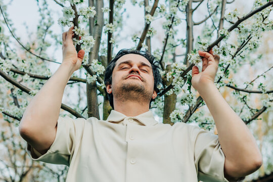 White European man in white shirt near blooming white tree enjoying spring allergy-free pollen