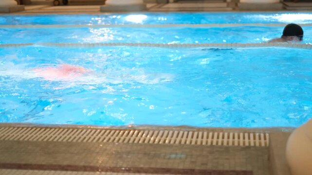 Two swimmers doing breaststroke toward each other in pool on parallel lanes