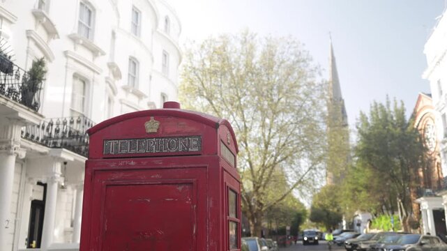 Traditional red telephone booth standing on a charming london street with classic architecture, showcasing an iconic british symbol against the backdrop of urban life
