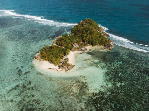 Aerial view of Anse L' Islette island with white sandy beaches and lush tropical vegetation surrounded by turquoise coral reefs Seychelles.