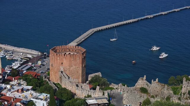 Historic coastal landscape with Alanya Red Tower, seaside fortress, offers panoramic views of bustling waterfront and harbor filled with boats. Kizil Kule. Travel and tourism concept.