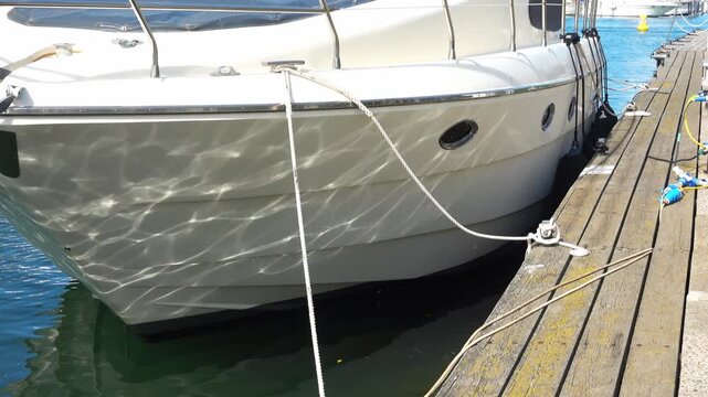 A white yacht is tied to a berth in a marina in calm water.
