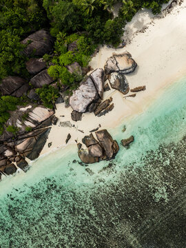 Aerial view of Takamaka beach featuring large granite boulders, white sand, and turquoise water over coral reefs in Takamaka, Seychelles.