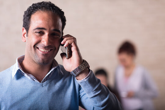 Young Middle Eastern entrepreneur smiling on phone in a creative coworking open space office with colleagues