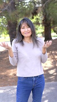 Cheerful mature woman looking at camera shrugging at viewer smiling communication concept vertical video bokeh background