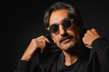 Obraz premium Confident man poses stylishly in dark attire and trendy sunglasses