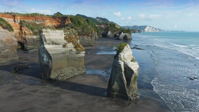 The stunning geological formations of the Three Sisters at Tongaporutu Beach, Taranaki, New Zealand, are sculpted by the Tasman Sea. This coastal landscape showcases layered cliffs and sea stacks