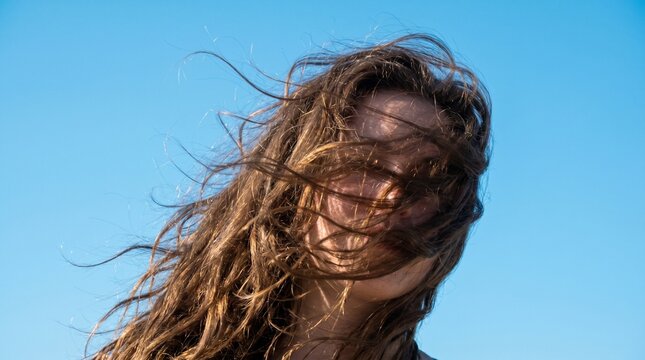 Wind-blown hair hiding face, dynamic motion strands, isolated sky blue background