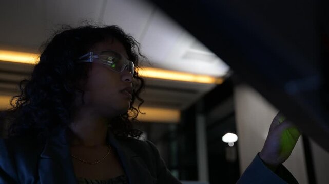 Focused female software developer pointing at complex database code on a large monitor in a dark office. Tech professional working late night analyzing data for an advanced cybersecurity project.