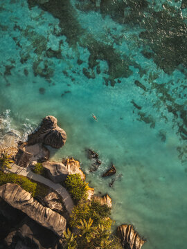 Aerial view of Anse Source d'Argent beach with turquoise water, granite boulders, coral reefs, and a person swimming in L'Union Estate, Seychelles.