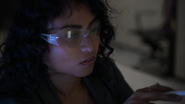 Focused female software developer pointing at complex database code on a large monitor in a dark office. Tech professional working late night analyzing data for an advanced cybersecurity project.