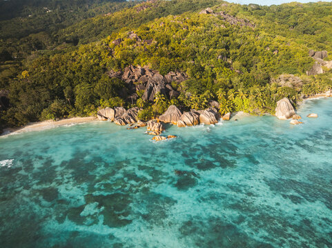 Aerial view of the iconic granite boulders and turquoise waters of Anse Source d'Argent beach surrounded by lush tropical forest L'Union Estate, Seychelles.