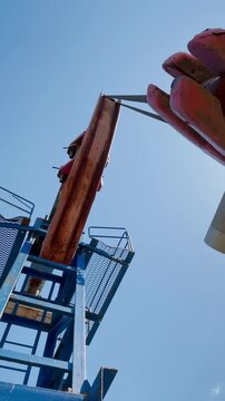 A girl stands atop a diving platform, preparing to jump into a pool. The blue sky frames the scene, highlighting the diving platform and the girl s anticipation.