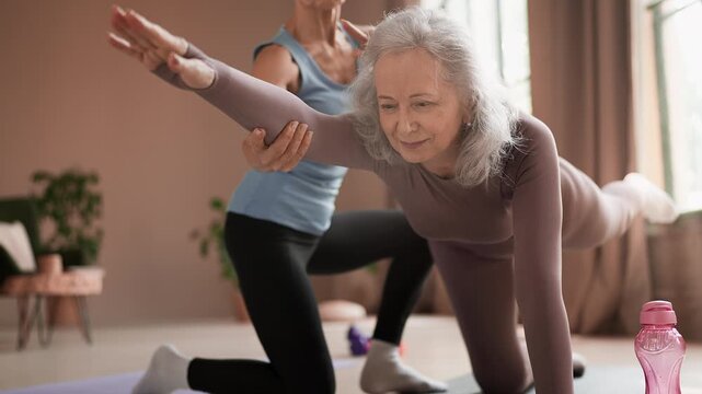 Senior woman practicing balancing table pose with trainer support in class