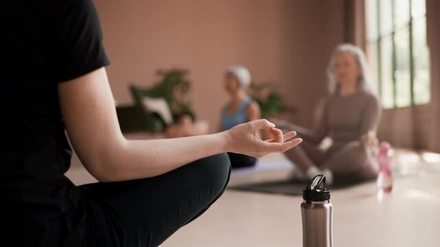 Senior women performing lotus pose and meditating with trainer in class