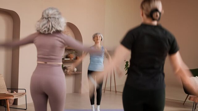 Slim senior female trainer leading cardio exercise with women in fitness class