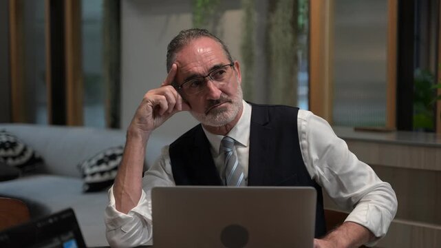 Focused senior business executive thinking deeply while analyzing corporate data on a laptop in a modern office. Mature entrepreneur solving complex problems and making strategic financial decisions.