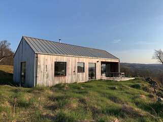 Fototapeta premium A bright Scandinavian-style wooden cabin stands on a green lawn in sunny daytime. It has light wood siding, metal roof and open sliding glass doors, presenting warm cozy minimalist pastoral rural aest