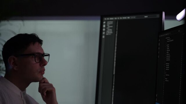 Focused young female software developer programming code on multiple monitors in a dark home office at night. Professional woman engineer working on cyber security and data science tech project.