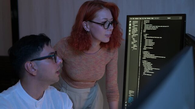Two software developers collaborating at night, focusing on code review and debugging process on a computer screen, representing teamwork, innovation, and modern software development workflow.