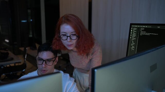 Two software developers collaborating at night, focusing on code review and debugging process on a computer screen, representing teamwork, innovation, and modern software development workflow.