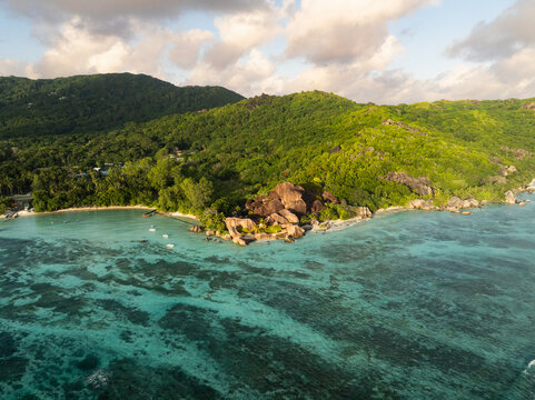 Aerial view of Anse Source d'Argent with its iconic granite boulders, turquoise waters, and lush tropical hills under a soft sky in L'Union Estate, Seychelles.