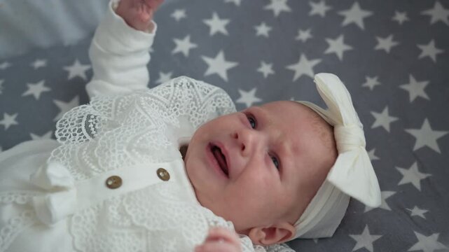 Close up distressed newborn baby wearing lace trimmed white clothing headband lying on star fabric promoting innocence vulnerability comfort and care. Infant child family love parenthood cozy home