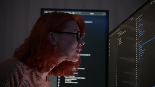 Focused female software developer coding at night in a modern workspace, wearing glasses and analyzing code on computer screen. Concept of programming, technology, cybersecurity, and digital innovatio